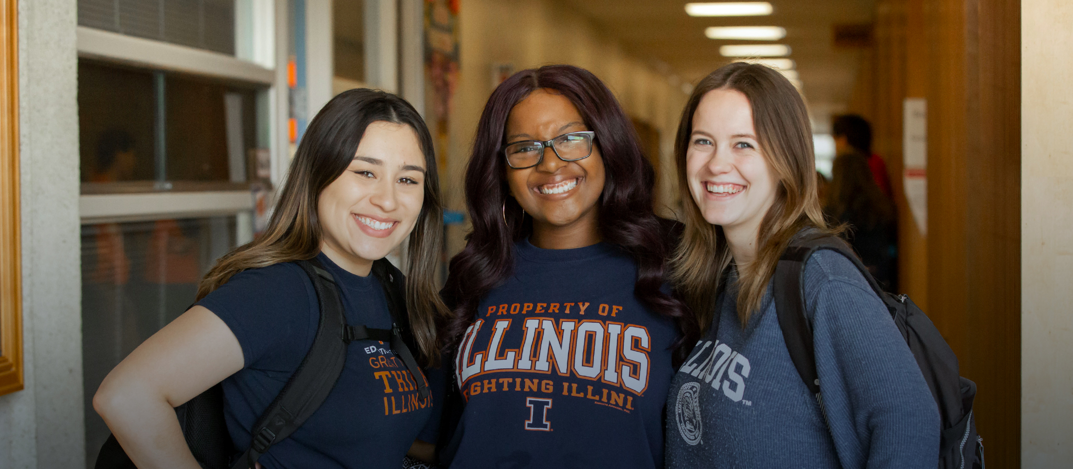 Image of three students smiling in the hallway